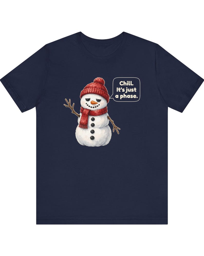 Pode incluir: Uma t-shirt azul-marinho de manga curta com o gr&aacute;fico de um boneco de neve a usar um gorro e um cachecol de malha vermelha. O boneco tem um nariz de cenoura, bra&ccedil;os de ramo e um bal&atilde;o com o texto: Chill. It's just a phase.