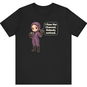 Puede incluir: Una camiseta negra de manga corta con una ilustraci&oacute;n de dibujos animados de una persona con traje de vuelo morado y botas marrones sosteniendo unas gafas. Un globo de texto junto al personaje contiene: I flew the Channel. Nobody noticed.