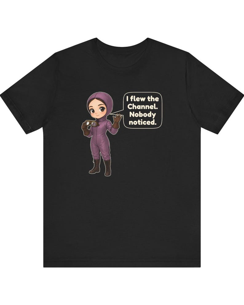 Puede incluir: Una camiseta negra de manga corta con una ilustraci&oacute;n de dibujos animados de una persona con traje de vuelo morado y botas marrones sosteniendo unas gafas. Un globo de texto junto al personaje contiene: I flew the Channel. Nobody noticed.
