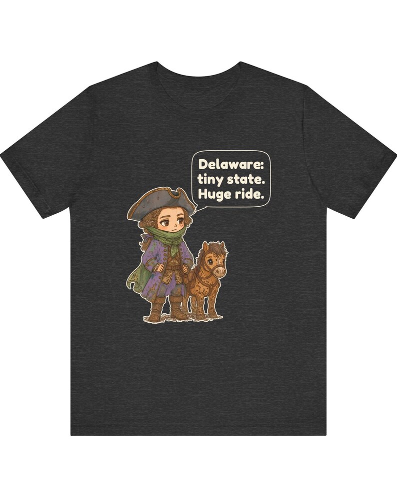 May include: A dark heather gray t-shirt featuring a cartoon illustration of a person in a tricorn hat and purple coat standing next to a small brown horse. A speech bubble contains the text: Delaware: tiny state. Huge ride.