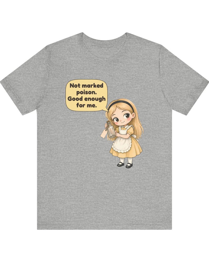 May include: A heather gray t-shirt featuring a cartoon illustration of a blonde character in a yellow dress and white apron holding a glass bottle. A speech bubble above the character contains the text: Not marked poison. Good enough for me.