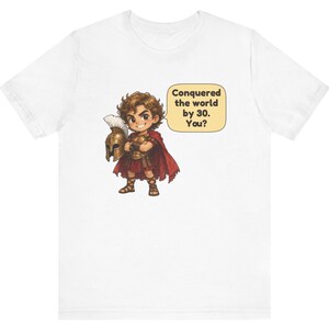 May include: A white t-shirt featuring a cartoon illustration of a warrior in bronze armor and a red cape, holding a plumed helmet. A speech bubble next to the character contains the text: Conquered the world by 30. You?