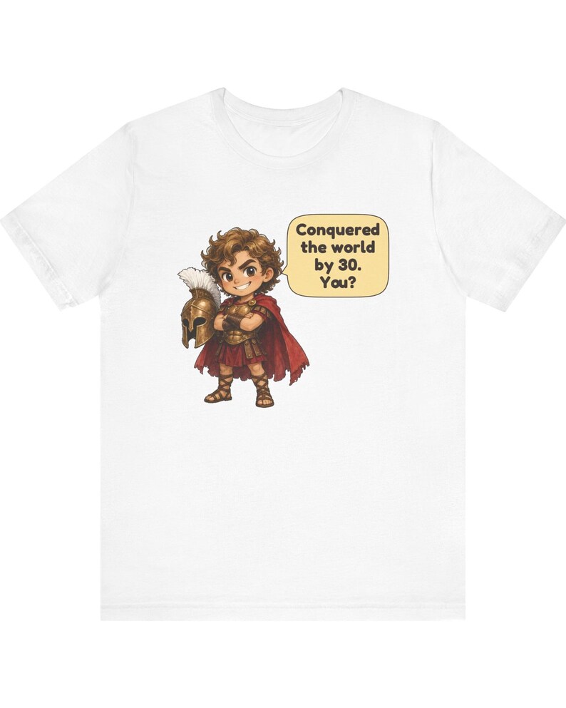 May include: A white t-shirt featuring a cartoon illustration of a warrior in bronze armor and a red cape, holding a plumed helmet. A speech bubble next to the character contains the text: Conquered the world by 30. You?