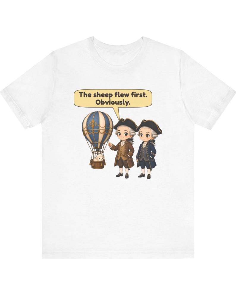 May include: A white t-shirt featuring a graphic of two figures in 18th-century attire standing next to a hot air balloon with a sheep in the basket. A speech bubble above them contains the text: The sheep flew first. Obviously.