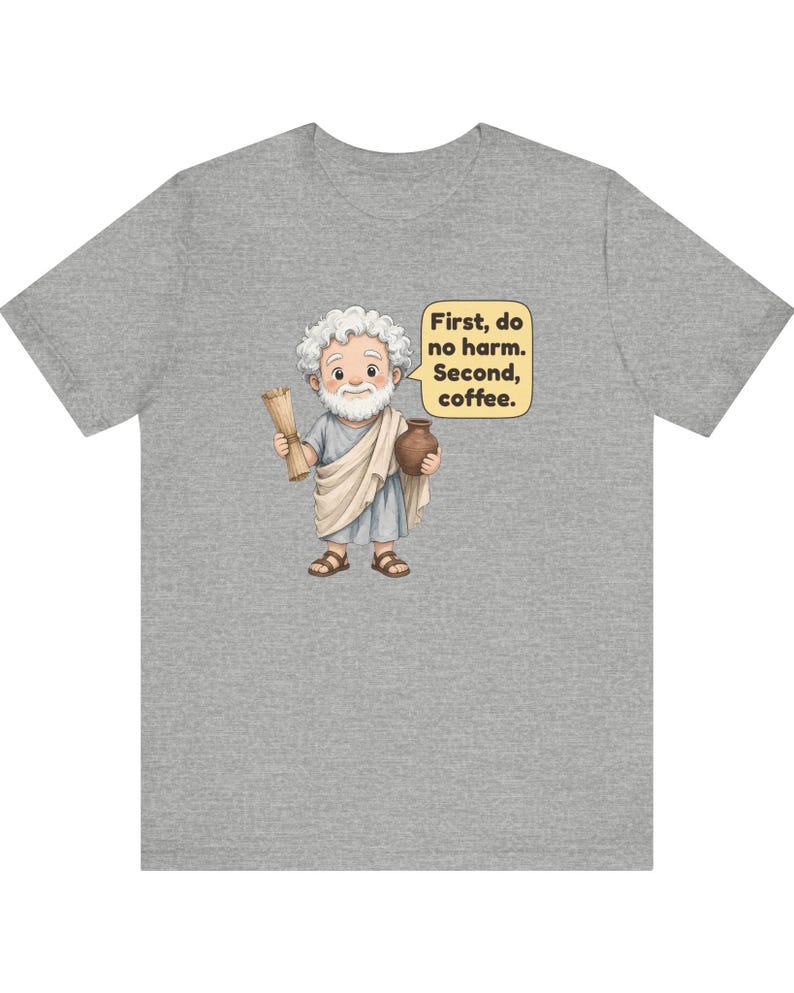 May include: A heather gray t-shirt featuring a cartoon illustration of an elderly person with white hair and a beard, wearing a light blue tunic and sandals. The figure holds a scroll and a brown pot, with a speech bubble stating: First, do no harm. Second, coffee.