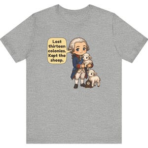 Peut inclure: Un t-shirt gris chin&eacute; avec une illustration de style dessin anim&eacute; repr&eacute;sentant un personnage historique en habit bleu du XVIIIe si&egrave;cle tenant un mouton blanc, accompagn&eacute; d'un autre mouton et d'une horloge. Texte : Lost thirteen colonies. Kept the sheep.