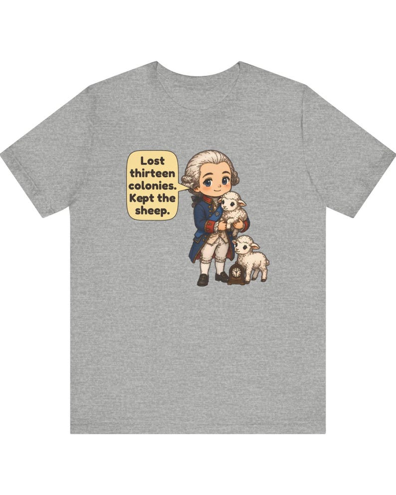 Peut inclure: Un t-shirt gris chin&eacute; avec une illustration de style dessin anim&eacute; repr&eacute;sentant un personnage historique en habit bleu du XVIIIe si&egrave;cle tenant un mouton blanc, accompagn&eacute; d'un autre mouton et d'une horloge. Texte : Lost thirteen colonies. Kept the sheep.