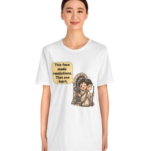 K&ouml;nnte beinhalten: Ein wei&szlig;es T-Shirt mit einer Grafik des zweigesichtigen r&ouml;mischen Gottes Janus vor einem Steinbogen. Ein Gesicht l&auml;chelt und h&auml;lt einen Schl&uuml;ssel, das andere wirkt ernst. Eine Sprechblase enth&auml;lt den Text: This face made resolutions. That one didn't.