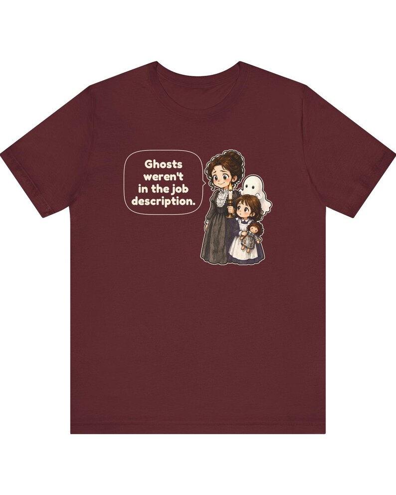 Op de afbeelding: Een bordeauxrood t-shirt met korte mouwen en een afbeelding van een persoon in een donkere jurk die een kaars vasthoudt, een kind en een klein spookje. Een tekstballon bevat de tekst: Ghosts weren't in the job description.