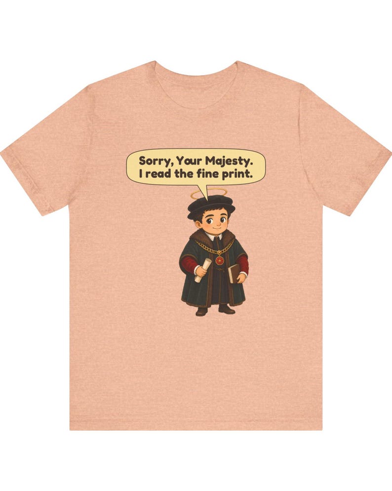 May include: A peach-colored t-shirt featuring a cartoon illustration of a figure in a dark robe, a gold chain, and a halo. A speech bubble above the figure contains the text: Sorry, Your Majesty. I read the fine print.