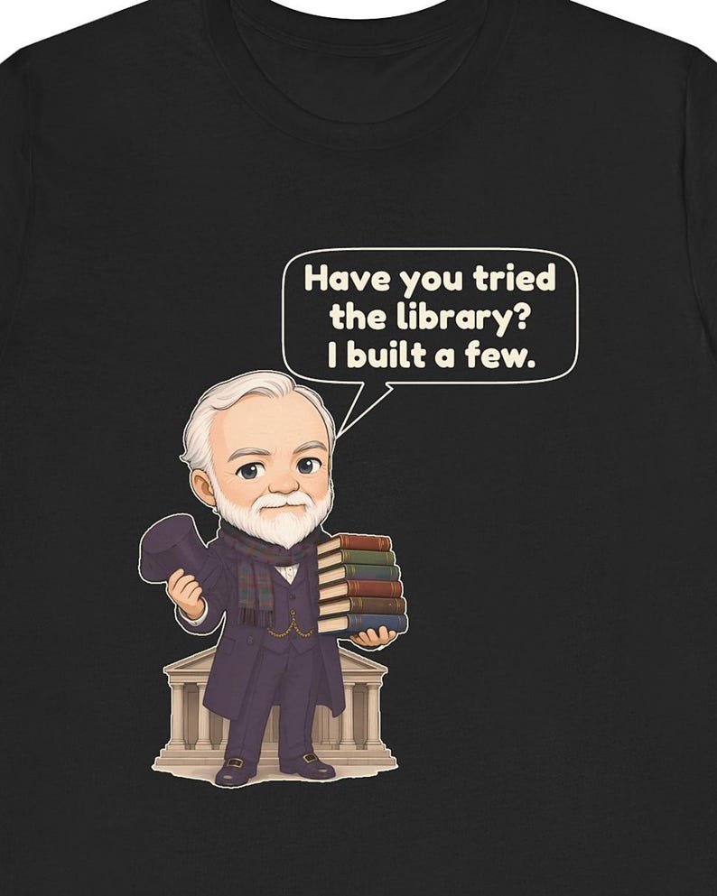 May include: A black t-shirt featuring a cartoon illustration of an older man with a white beard, wearing a dark coat and scarf, holding a top hat and a stack of books. A speech bubble contains the text: Have you tried the library? I built a few.