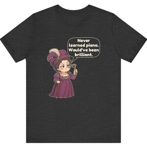 May include: A dark heather gray t-shirt featuring a cartoon illustration of a person in a purple Victorian-style dress, hat, and pearls, holding a monocle. A speech bubble contains the text: Never learned piano. Would've been brilliant.