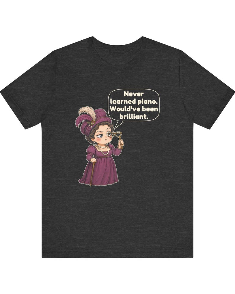 May include: A dark heather gray t-shirt featuring a cartoon illustration of a person in a purple Victorian-style dress, hat, and pearls, holding a monocle. A speech bubble contains the text: Never learned piano. Would've been brilliant.