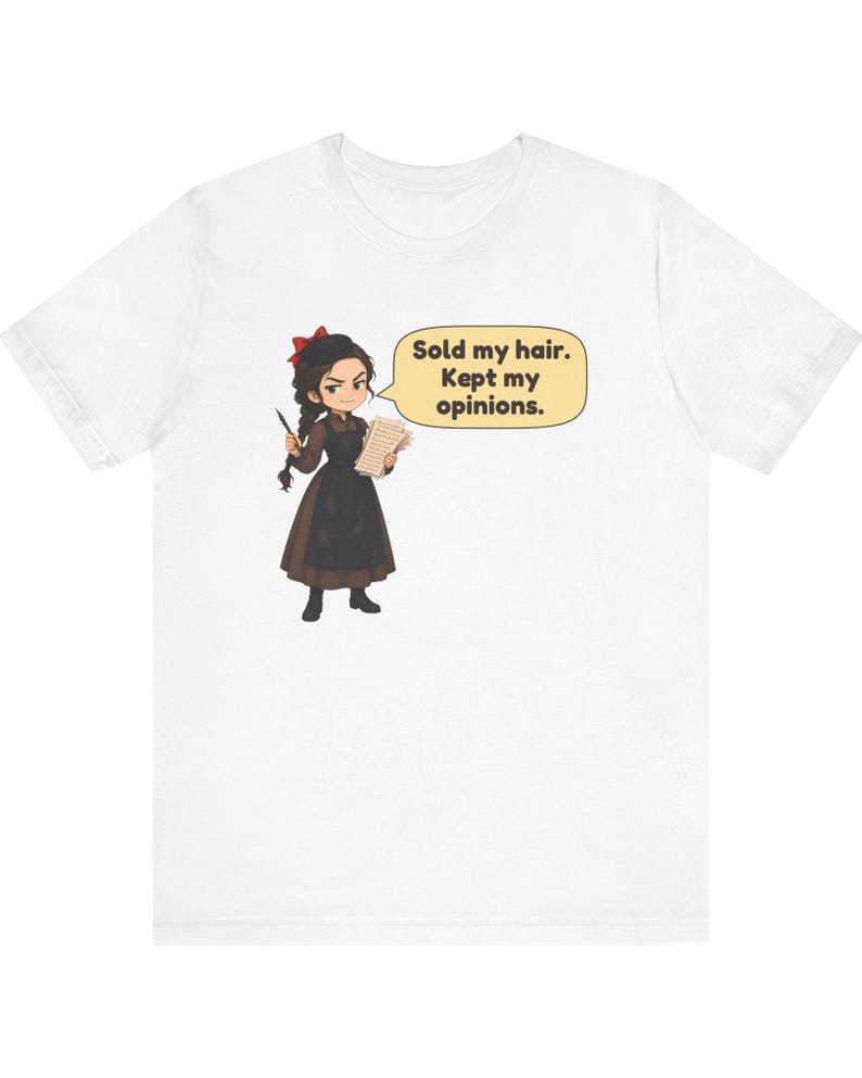 May include: A white t-shirt featuring a cartoon illustration of a person with dark braided hair, wearing a brown dress and black apron, holding a quill and paper. A speech bubble contains the text: Sold my hair. Kept my opinions.