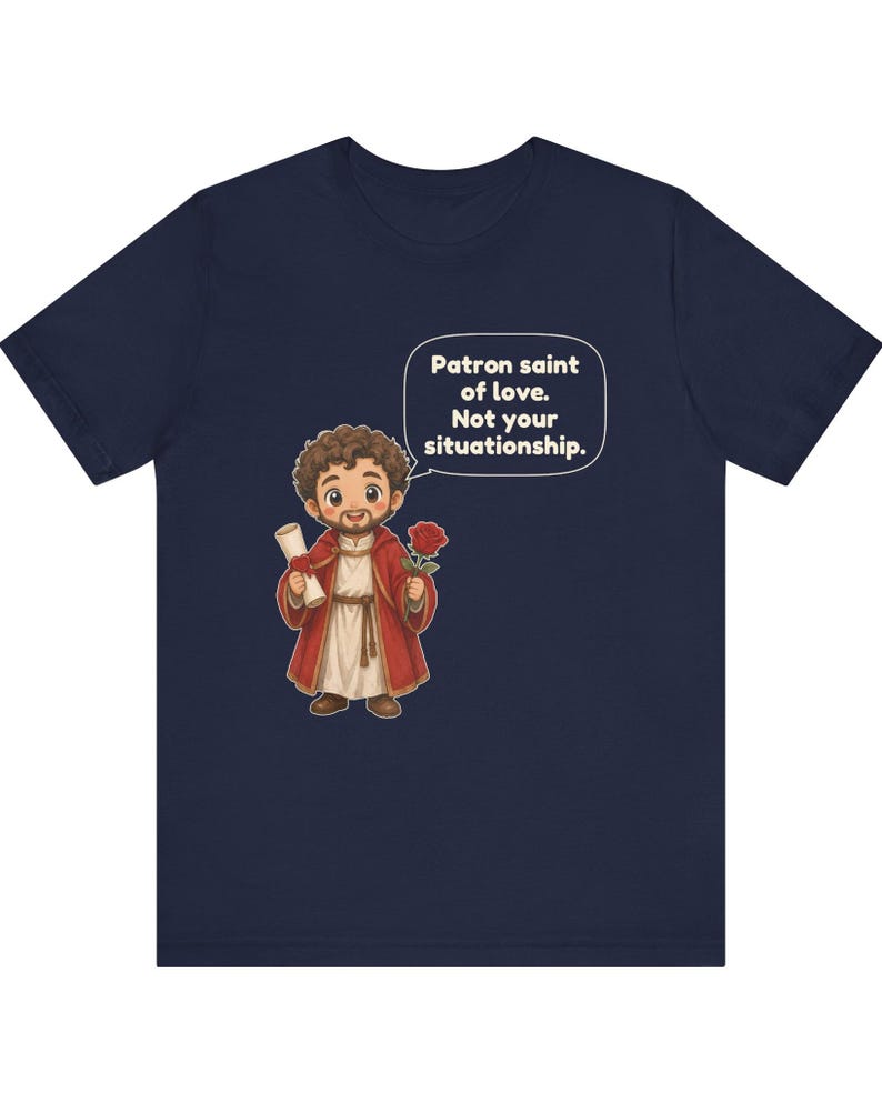 Puede incluir: Una camiseta azul marino con una ilustraci&oacute;n de dibujos animados de una figura barbuda con t&uacute;nica roja que sostiene un pergamino y una rosa roja. Un globo de texto sobre la figura contiene el texto: Patron saint of love. Not your situationship.
