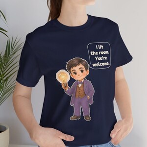 Może przedstawiać: Granatowy t-shirt z rysunkową ilustracją osoby w fioletowym garniturze i brązowej kamizelce, trzymającej świecącą żar&oacute;wkę. Dymek z tekstem zawiera napis: I lit the room. You're welcome.