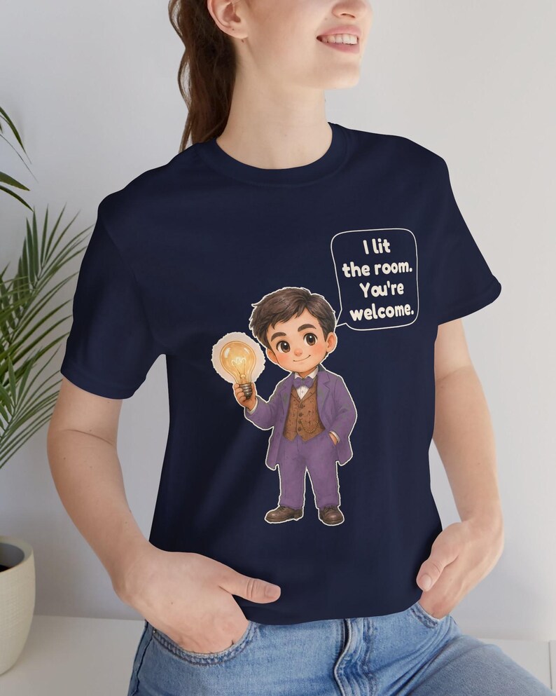Może przedstawiać: Granatowy t-shirt z rysunkową ilustracją osoby w fioletowym garniturze i brązowej kamizelce, trzymającej świecącą żar&oacute;wkę. Dymek z tekstem zawiera napis: I lit the room. You're welcome.
