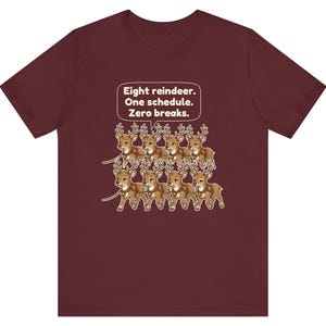 K&ouml;nnte beinhalten: Ein bordeauxrotes Kurzarm-T-Shirt mit einer Grafik von acht braunen Rentieren in zwei Reihen mit Geschirren. &Uuml;ber den Rentieren befindet sich eine wei&szlig;e Sprechblase mit dem Text: Eight reindeer. One schedule. Zero breaks.