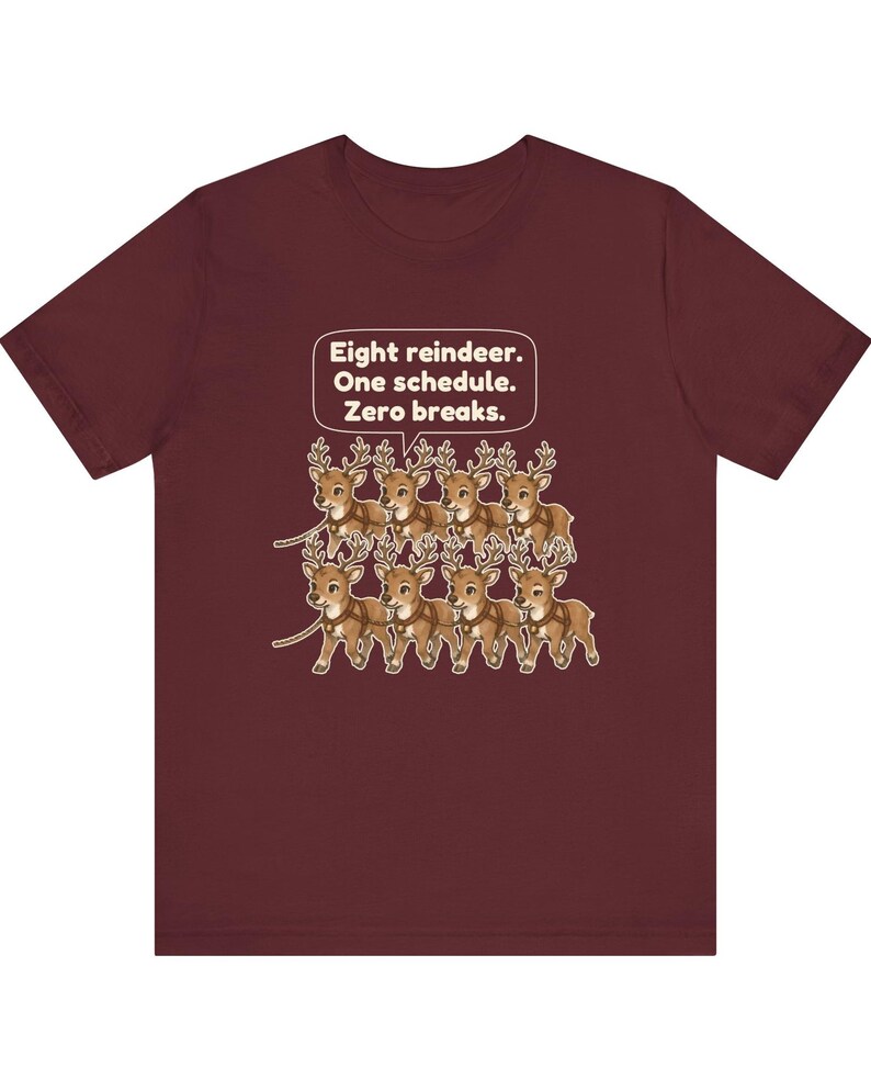K&ouml;nnte beinhalten: Ein bordeauxrotes Kurzarm-T-Shirt mit einer Grafik von acht braunen Rentieren in zwei Reihen mit Geschirren. &Uuml;ber den Rentieren befindet sich eine wei&szlig;e Sprechblase mit dem Text: Eight reindeer. One schedule. Zero breaks.