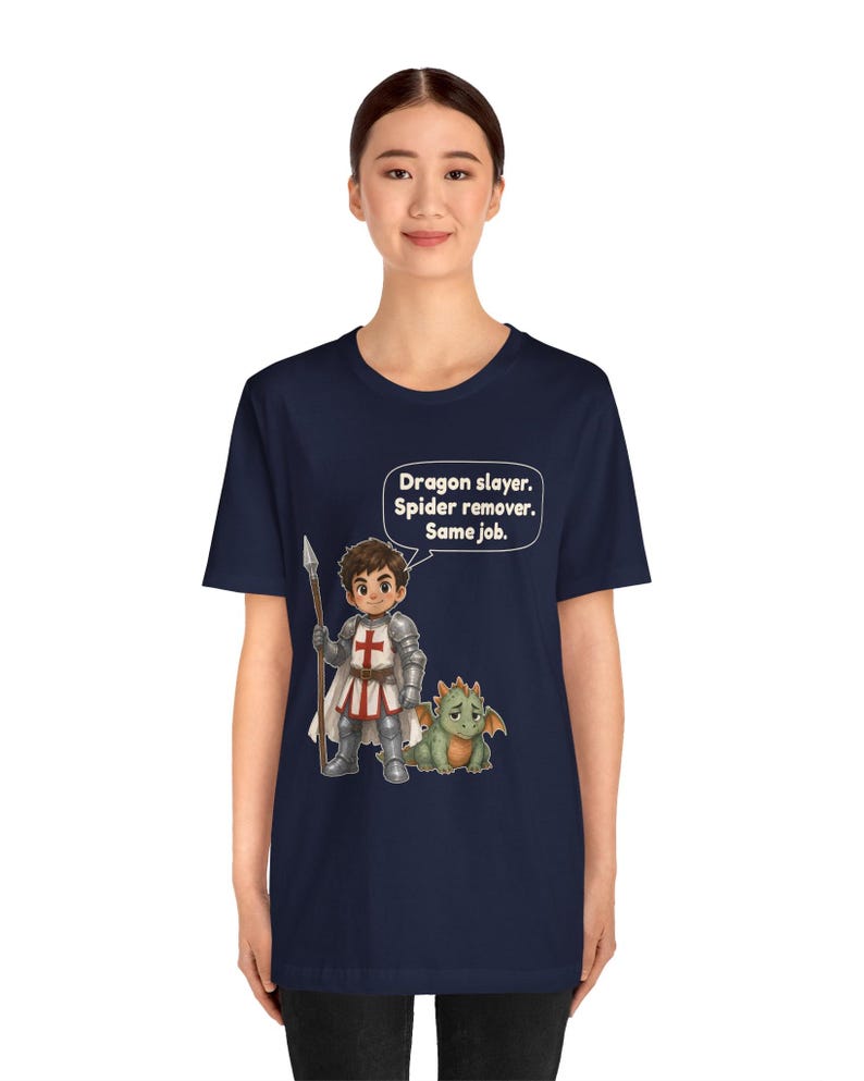 K&ouml;nnte beinhalten: Ein marineblaues T-Shirt mit einer Grafik eines Ritters in silberner R&uuml;stung, der einen Speer h&auml;lt, und einem kleinen gr&uuml;nen Drachen. Dar&uuml;ber befindet sich eine Sprechblase mit dem Text: Dragon slayer. Spider remover. Same job.