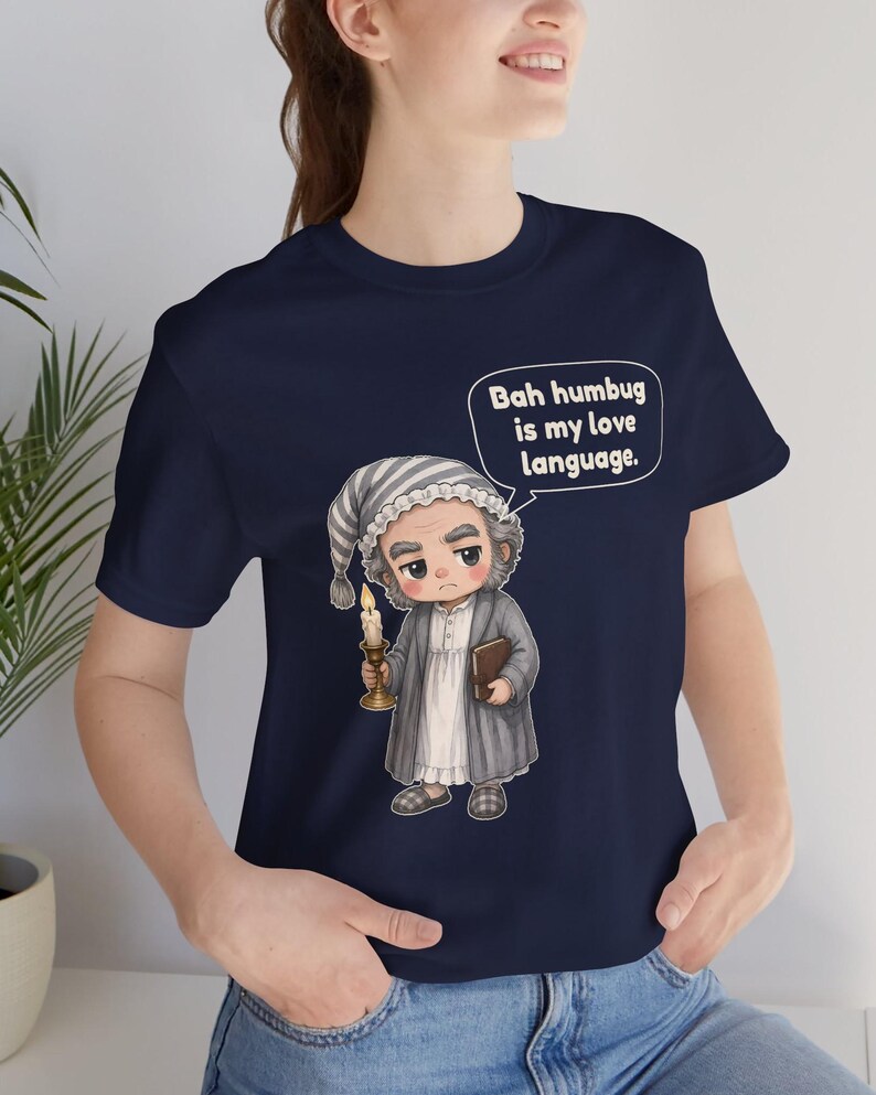 Puede incluir: Una camiseta azul marino con el gr&aacute;fico de un personaje con gorro de dormir y bata a rayas, sosteniendo una vela encendida y un libro. Un globo de texto contiene la frase: Bah humbug is my love language.