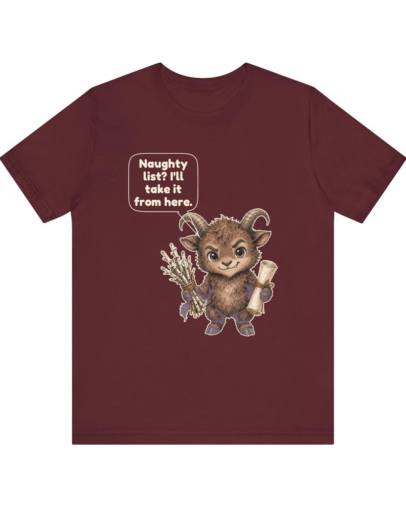 Puede incluir: Una camiseta de manga corta color granate con el gr&aacute;fico de una peque&ntilde;a criatura peluda con cuernos que sostiene un manojo de palos y un pergamino. Un bocadillo sobre la criatura contiene el texto: Naughty list? I'll take it from here.