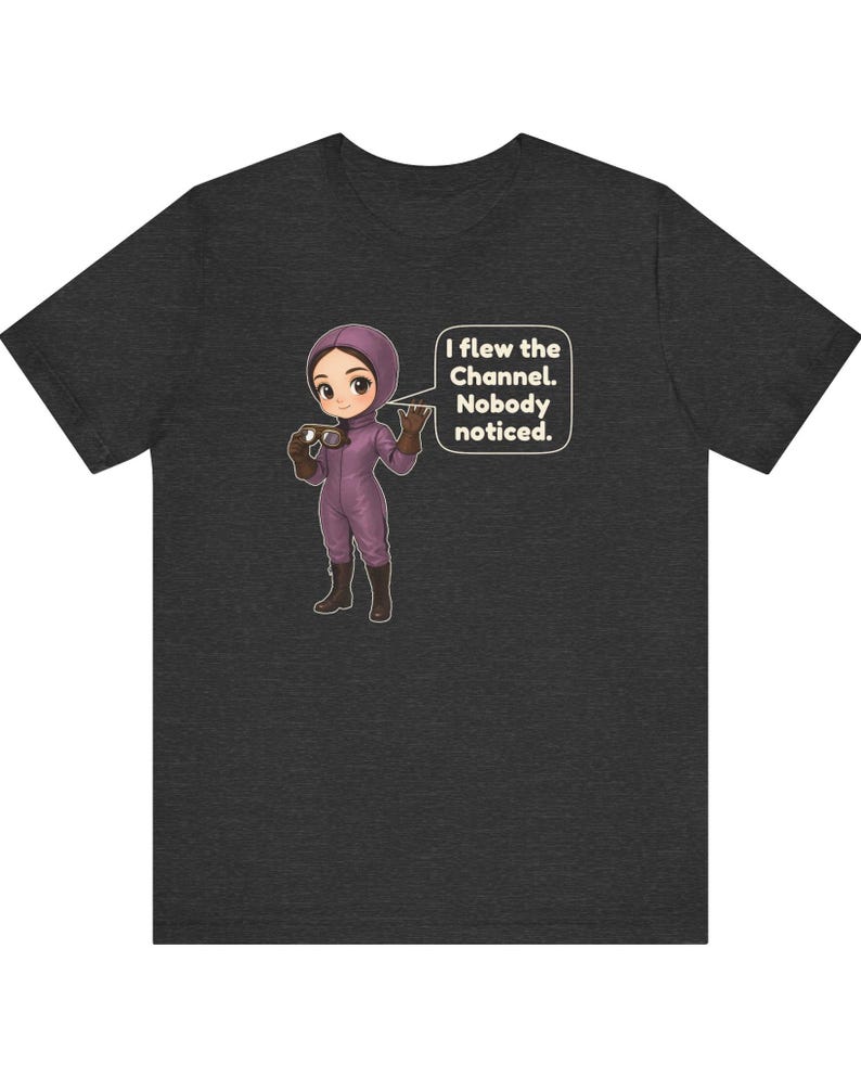 Puede incluir: Una camiseta gris oscuro con una ilustraci&oacute;n de dibujos animados de una persona con traje de vuelo morado y gafas. Un globo de texto junto al personaje contiene el texto: I flew the Channel. Nobody noticed.