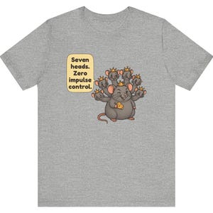 May include: A heather gray t-shirt featuring a graphic of a seven-headed rat wearing small gold crowns and holding a piece of yellow cheese. A speech bubble next to the rat contains the text: Seven heads. Zero impulse control.
