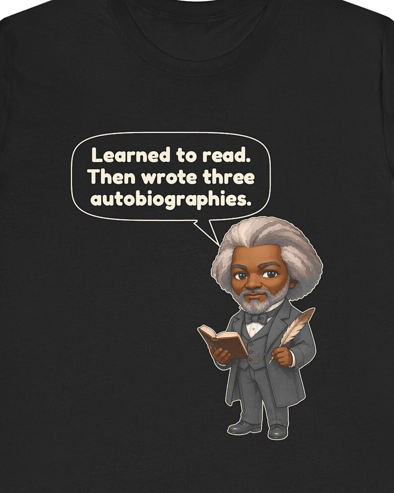 Puede incluir: Una camiseta negra con una ilustraci&oacute;n estilo caricatura de Frederick Douglass sosteniendo un libro y una pluma. Un globo de texto sobre &eacute;l contiene el texto: Learned to read. Then wrote three autobiographies. El dise&ntilde;o est&aacute; centrado.