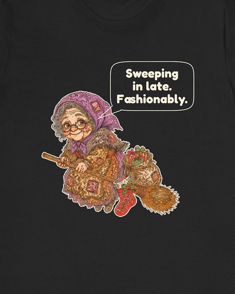 Puede incluir: Una camiseta negra con el gr&aacute;fico de una persona mayor con pelo gris, gafas y pa&ntilde;uelo morado montada en una escoba. La persona viste un vestido estampado y lleva un saco de regalos y un calcet&iacute;n rojo. El texto dice: Sweeping in late. Fashionably.