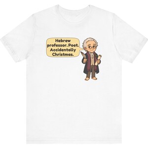Pu&ograve; includere: Una t-shirt bianca a maniche corte con un'illustrazione a cartone animato di una persona anziana con capelli grigi, occhiali tondi e un cappotto scuro. Un fumetto contiene il testo: Hebrew professor. Poet. Accidentally Christmas.
