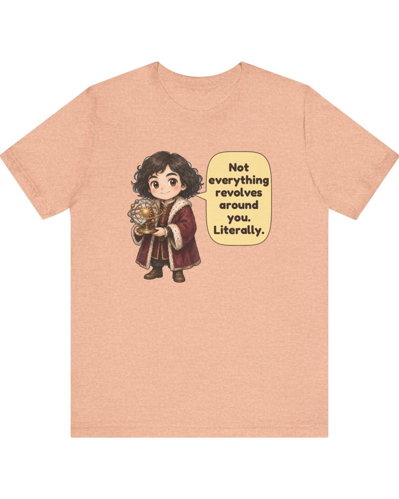 May include: A peach-colored t-shirt featuring a cartoon illustration of a person in historical clothing holding a model of the solar system. A speech bubble next to the figure contains the text: Not everything revolves around you. Literally.