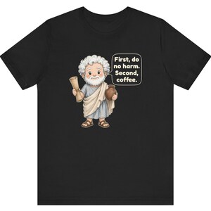 May include: A black short-sleeve t-shirt featuring a cartoon illustration of a bearded figure in a light blue tunic and white toga, holding a scroll and a brown pot. A speech bubble contains the text: First, do no harm. Second, coffee.