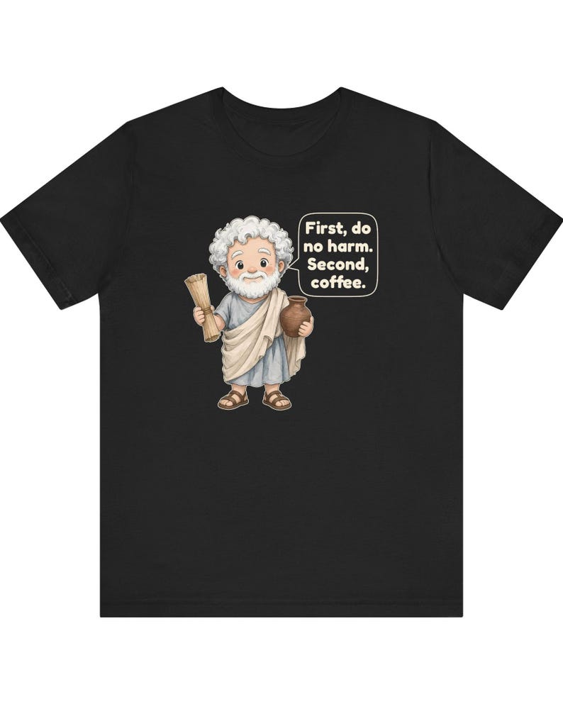 May include: A black short-sleeve t-shirt featuring a cartoon illustration of a bearded figure in a light blue tunic and white toga, holding a scroll and a brown pot. A speech bubble contains the text: First, do no harm. Second, coffee.