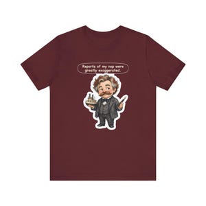 Watercolor chibi Mississippi riverboat author with a bushy moustache, navy bow tie and charcoal suit, holding a model riverboat and a fountain pen, with the speech bubble "Reports of my nap were greatly exaggerated." printed on a tee