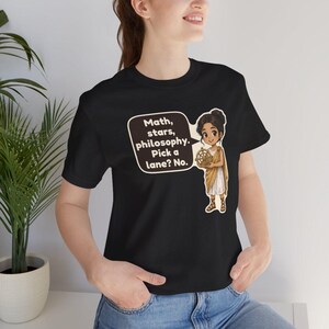 May include: A black short-sleeved t-shirt featuring a cartoon illustration of a person in a tan toga holding an astrolabe. A speech bubble next to the figure contains the text: Math, stars, philosophy. Pick a lane? No.
