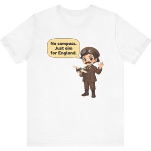 May include: A white t-shirt featuring a cartoon illustration of an aviator with a mustache, goggles, and a brown suit holding a small airplane. A speech bubble contains the text: No compass. Just aim for England.
