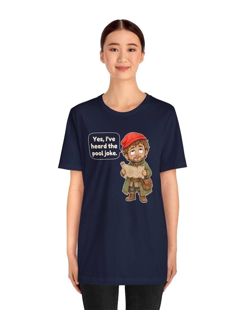 May include: A navy blue short-sleeve t-shirt featuring a cartoon illustration of a character wearing a red cap and green coat, holding a map. A speech bubble above the character contains the text, "Yes, I've heard the pool joke."