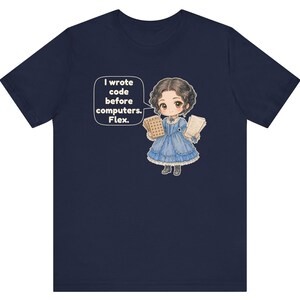 May include: A navy blue t-shirt featuring a cartoon illustration of a person in a blue Victorian-style dress holding punch cards and papers. A speech bubble next to the figure contains the text: I wrote code before computers. Flex.