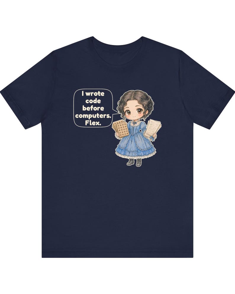 May include: A navy blue t-shirt featuring a cartoon illustration of a person in a blue Victorian-style dress holding punch cards and papers. A speech bubble next to the figure contains the text: I wrote code before computers. Flex.