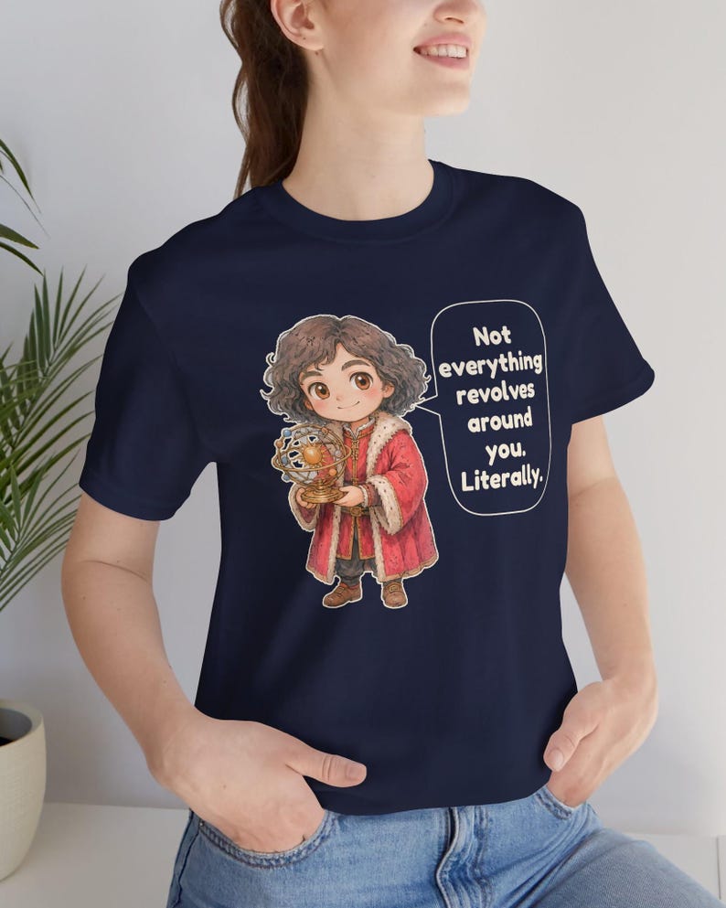 May include: A navy blue t-shirt featuring a cartoon character with curly brown hair wearing a red coat with fur trim, holding a model of the solar system. A speech bubble contains the text: Not everything revolves around you. Literally.