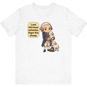 Peut inclure: Un t-shirt blanc avec une illustration de style dessin anim&eacute; repr&eacute;sentant un personnage historique en manteau bleu et perruque blanche tenant un agneau, avec un autre agneau et une petite horloge. Une bulle contient le texte : Lost thirteen colonies. Kept the sheep.