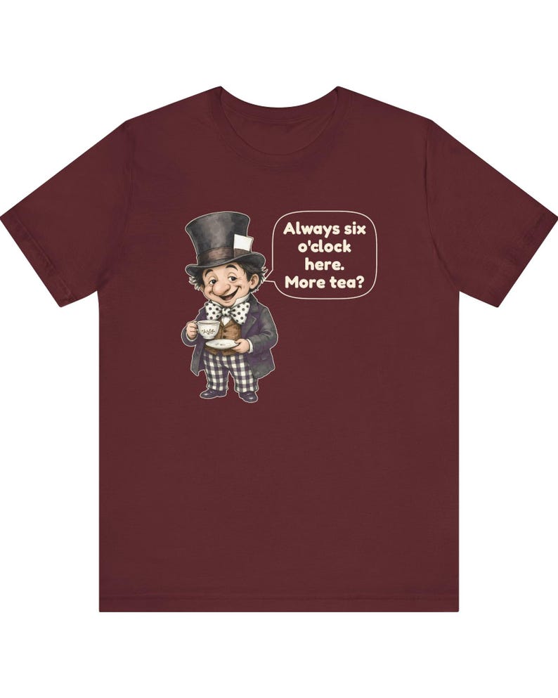 May include: A maroon t-shirt featuring a graphic of a character wearing a top hat, a polka-dot bow tie, and checkered trousers, holding a teacup and saucer. A speech bubble next to the character contains the text: Always six o'clock here. More tea?