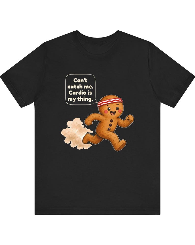 May include: A black t-shirt featuring a cartoon gingerbread person wearing a red and white striped headband, running and leaving a dust cloud behind. A speech bubble above the character contains the text: Can't catch me. Cardio is my thing.