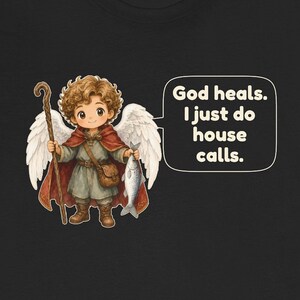 May include: A black t-shirt featuring a cartoon angel with curly brown hair, white wings, a red cloak, and a brown tunic. The angel holds a wooden staff and a silver fish. A speech bubble contains the text: God heals. I just do house calls.