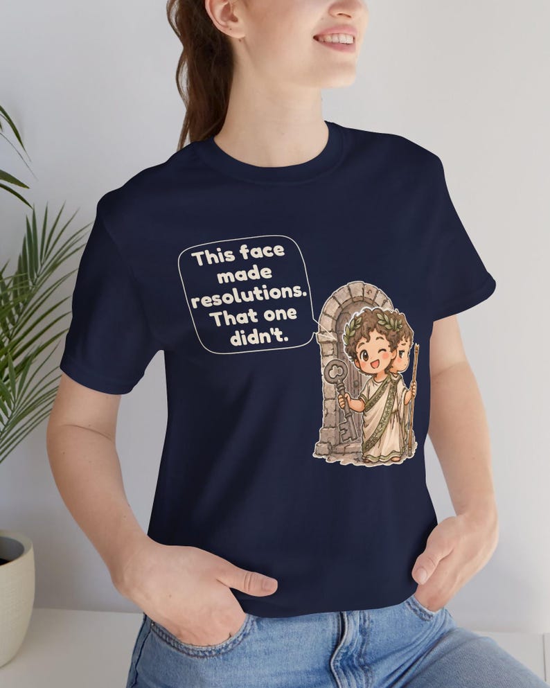 K&ouml;nnte beinhalten: Ein marineblaues T-Shirt mit einer Grafik einer r&ouml;mischen Figur mit zwei Gesichtern, die einen Lorbeerkranz tr&auml;gt und einen Schl&uuml;ssel sowie einen Stab vor einem Torbogen h&auml;lt. Eine Sprechblase enth&auml;lt den Text: This face made resolutions. That one didn't.