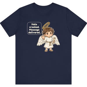 May include: A navy blue t-shirt featuring a graphic of a cartoon angel with brown hair, white wings, and a gold halo. The angel holds a scroll and waves. A speech bubble contains the text: Halo crooked. Message delivered.