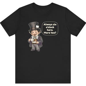May include: A black t-shirt featuring a graphic of a character wearing a top hat, a brown jacket, and checkered pants, holding a teacup and saucer. A speech bubble next to the character contains the text: Always six o'clock here. More tea?