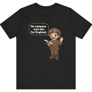 May include: A black t-shirt featuring a cartoon illustration of a pilot in a brown suit and aviator cap holding a small airplane. A speech bubble contains the text: No compass. Just aim for England. The pilot has a mustache and goggles.