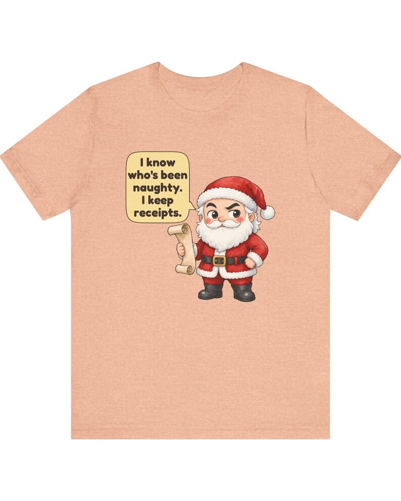 May include: A peach-colored t-shirt featuring a cartoon Santa Claus holding a scroll. A speech bubble next to Santa contains the text: I know who's been naughty. I keep receipts. The design is centered on the front of the short-sleeved crew neck shirt.